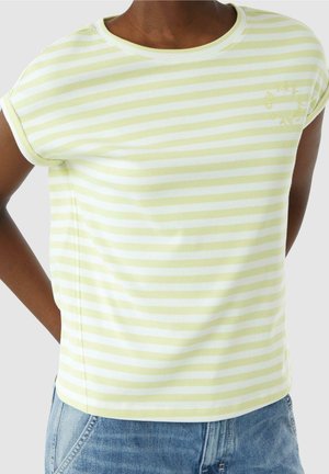 Persoon draagt een T-shirt met korte mouwen, lichtgroen en witte horizontale strepen, met opgerolde mouwen en lichtblauwe spijkerbroek.