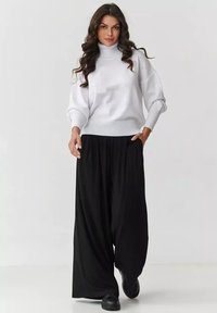 Biały sweter z golfem, z prążkowanymi mankietami i dołem, w połączeniu z luźnymi czarnymi spodniami. Całość dopełniają czarne obuwie.