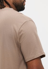 Khakinvärinen lyhythihainen t-paita pyöreällä pääntiellä, pehmeää puuvillaa, sileä pinta ja litteät saumat olkapäillä.