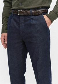Granatowe, dopasowane spodnie z teksturowanej tkaniny, zestawione z brązowym, plecionym skórzanym paskiem z metalową klamrą w kolorze srebrnym.