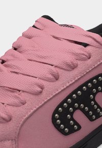 Κοντινό πλάνο σε ροζ σουέντ αθλητικό παπούτσι με παχιά ροζ κορδόνια και μαύρο διακοσμητικό έμπλαστρο διακοσμημένο με ασημένιες βούλες.