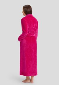 Bata de felpa fucsia con cuello de chal, cinturón en la cintura, mangas largas y bolsillos, que llega hasta los tobillos con una textura suave.