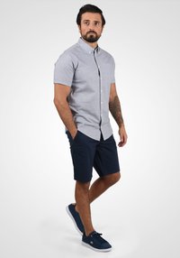 Short-sleeve, light blue button-up shirt, with a pocket, paired with navy shorts and navy suede sneakers. Casual fit and smooth texture.
