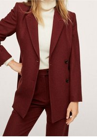 Bordeaux dubbelzijdige blazer in textuurstof, met zwarte knopen en geknipte revers, gecombineerd met een crèmekleurige coltrui eronder.