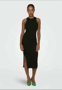 Robe noire sans manches avec une fente sur le côté, design ajusté et texture lisse, associée à des chaussures à talons hauts vertes. Simple et élégante.
