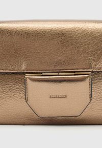 Clutch i metallisk gullfarget skinn med en teksturert overflate, utstyrt med en knappestenging og en synlig varemerkelogo preget på forsiden.