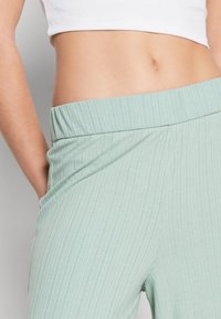 Lichtgroene ribbelbroek met een brede elastische tailleband en zijzakken, met een gladde, gemêleerde stof.