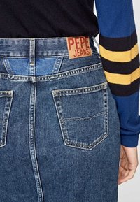 Jeanskjol med mörk tvätt, med två bakfickor och en läderetikett "PEPE JEANS" på midjebandet, visad bakifrån.