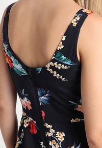 Mörkblå blommig klänning med låg rygg, försedd med justerbara band, flerfärgade blommor och en dold dragkedja längs backens söm.