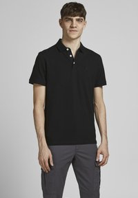 Zwart polo shirt van katoen, met een klassieke kraag, een placket met twee knopen en een subtiel logo op de borst. Draagt in combinatie met donkergrijze cargobroek.