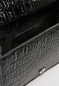 Borsa nera in pelle sintetica con stampa a coccodrillo, con una finitura lucida, caratterizzata da una chiusura con calamita e un interno in tessuto morbido.