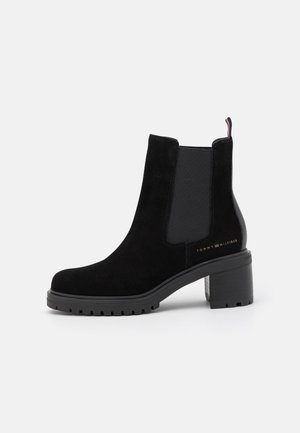 Bottines en suède noir avec panneaux élastiques sur les côtés, talon en caoutchouc noir épais et détail en or sur le côté. Texture lisse et design classique.