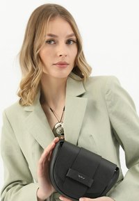 Czarna skórzana torebka o okrągłym kształcie, fakturowanym wykończeniu i przedniej klapce. Charakteryzuje się minimalistycznym designem i małym logo.