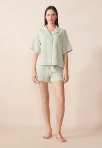 Lys grønn, kortermet skjorte med knapper og lomme, kombinert med matchende shorts. Begge laget av teksturert stoff. Enkel, avslappet design.