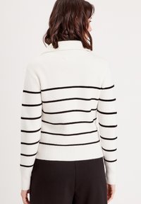 Pull en maille blanche avec des rayures noires horizontales. Il présente un col haut et des poignets ajustés, conçu pour un ajustement près du corps.