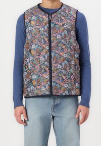 Blommönstrad ärmlös väst med marinblå bakgrund och flerfärgade blommor, dragkedjestängning och kontrasterande marinblå kant.