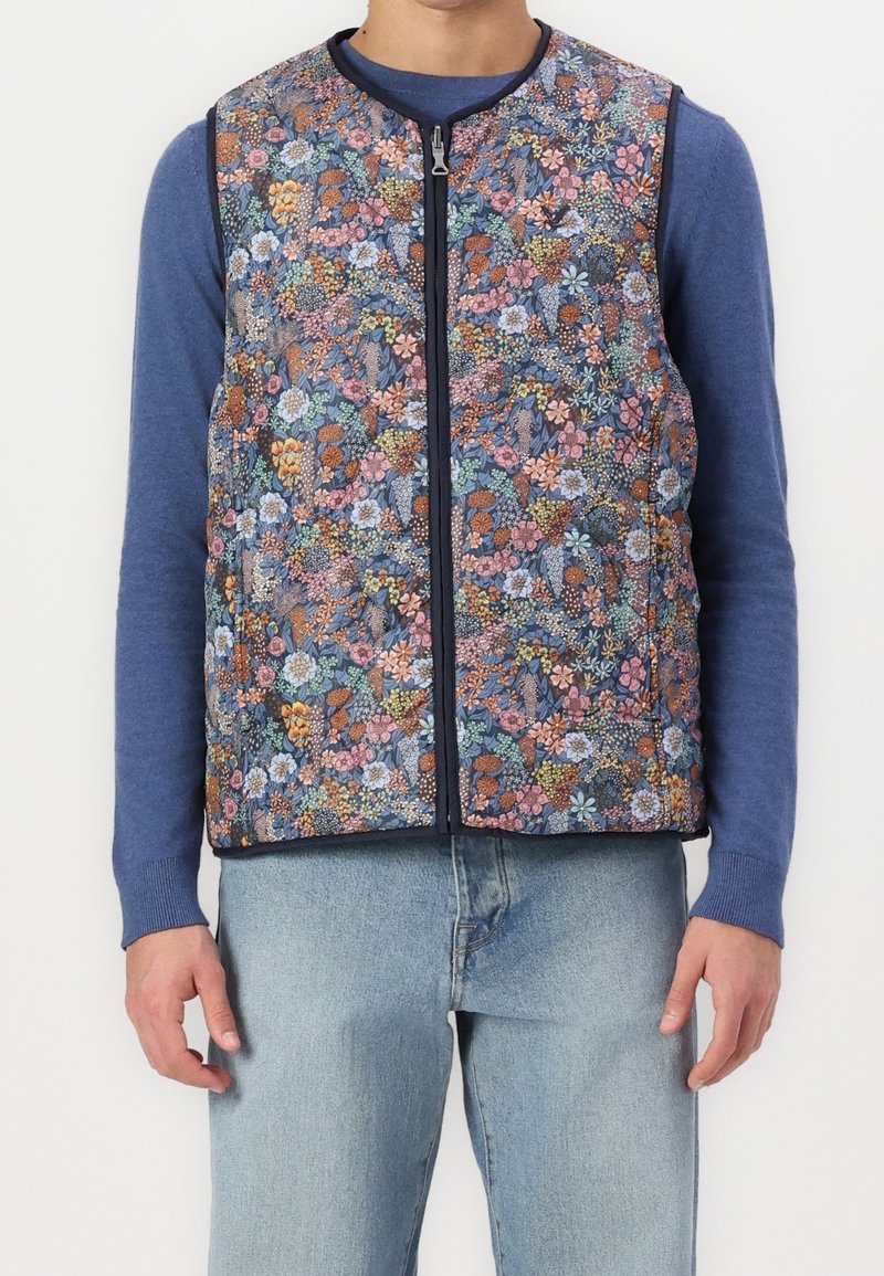 Blommönstrad ärmlös väst med marinblå bakgrund och flerfärgade blommor, dragkedjestängning och kontrasterande marinblå kant.