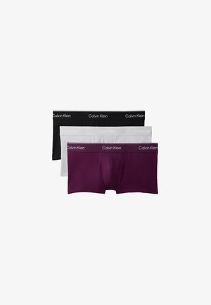 Homme torse nu portant un boxer Calvin Klein violet foncé, debout pieds nus sur un fond gris uni, les mains dans le dos.