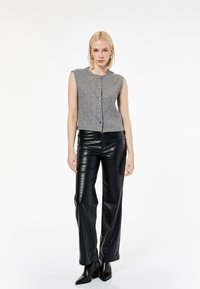 Grijs mouwloos ribgebreid topje met knopen aan de voorkant, gecombineerd met glanzende zwarte nepleer broek met een gestructureerd patroon, en zwarte enkelboots.