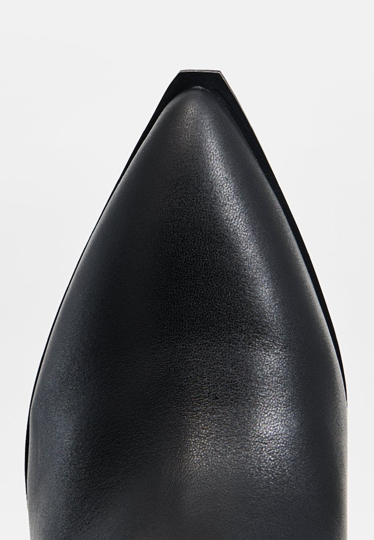 Zapato de cuero negro con punta afilada y textura suave. Presenta un sutil patrón de grano y un diseño elegante y minimalista.