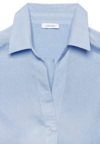 Camisa de color azul claro con un tejido ligeramente texturizado, que presenta un escote en V profundo y un solo botón en el cuello. Etiqueta de la marca visible.