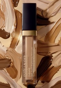 Estee Lauder Futurist Soft Touch Brightening Skincealer; transparent tube med svart lock; gulddetalj; omgiven av olika nyanser av kräm och brunt.
