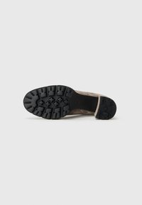 Botte en daim brun avec une semelle en caoutchouc noir texturé présentant un motif de semelle multidirectionnel pour une traction optimale. Design minimaliste et détails de coutures.