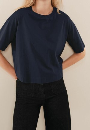 Navy blue, short-sleeved cotton t-shirt with a crew neckline, featuring a relaxed fit and minimal stitching detail. Paired with high-waisted black jeans.
