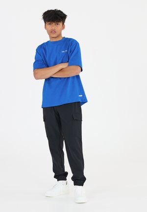 Blauwe katoenen T-shirt met korte mouwen en zwarte cargobroek met zijzakken, gecombineerd met witte sneakers. Eenvoudig ontwerp, relaxte pasvorm.