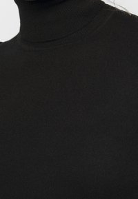 Gros plan sur un pull à col roulé noir en maille côtelée couvrant le cou et le haut de la poitrine.