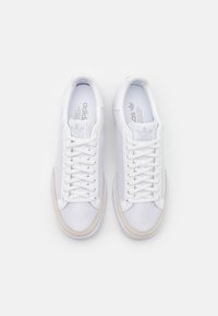 Bílé tenisky s texturovaným horním dílem z látky, vybavené světle béžovou gumovou podrážkou a bílými tkaničkami. Logo "adidas" světle šedé barvy.