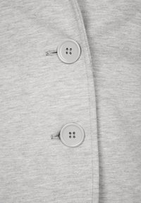 Szary, teksturowany materiał z dwoma okrągłymi guzikami czterodziurkowymi na plisce. Prosty krój z starannymi detalami przeszyć.