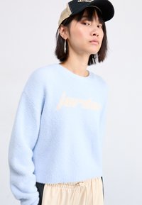 Lys blått, fuzzy gensere med en kort design og ordet "jordan" i myk ferskenstrikk. Kombinert med beige bukser med elastisk midje.