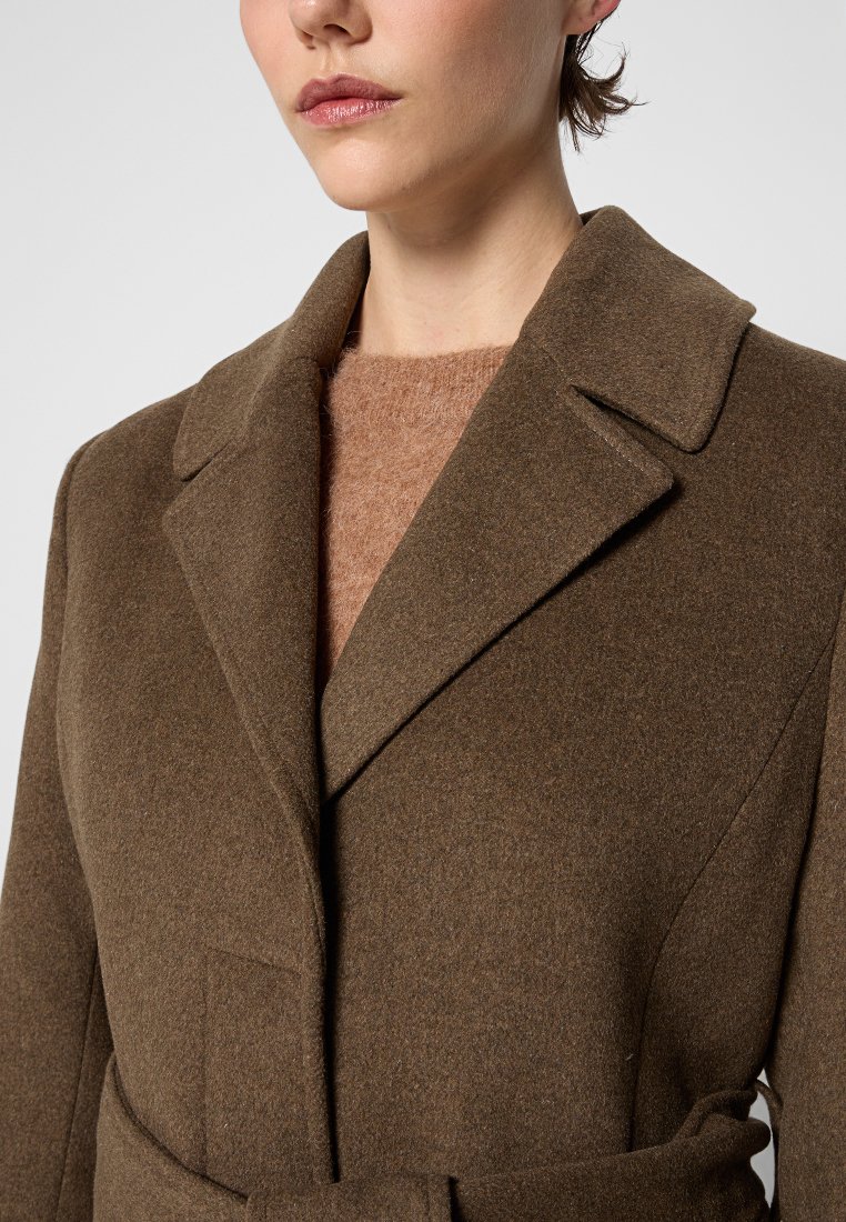 Brauner Wollmix-Mantel mit Reverskragen, einer Fronttasche und einem Gürtel, der in der Taille gebunden ist. Getragen über einem hellbraunen Pullover.
