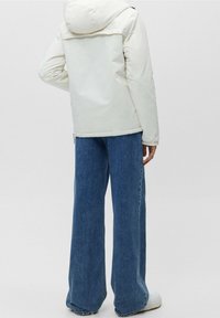 Vit puffjacka med huva, med en slät textur och praktisk design, tillsammans med vida blå denimjeans och vita sneakers.