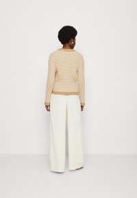 Maglione a righe in beige e crema con maniche lunghe, abbinato a pantaloni bianchi a gamba larga con pieghe. Tessuto a maglia, polsini e orlo a costine.