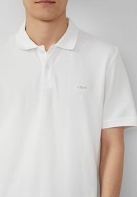 Weißes Polohemd aus strukturiertem Stoff, mit klassischem Kragen, Drei-Knopf-Leiste und kleinem gesticktem Logo auf der Brust.