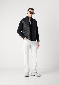 Μαύρο γιλέκο με επένδυση και υψηλό γιακά, με φανέλα μακρυμάνικη σε μαύρο χρώμα από κάτω. Συνδυάζεται με λευκά παντελόνια ίσια και γκρίζα αθλητικά παπούτσια.