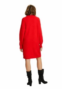 Czerwona dzianinowa sukienka z długimi rękawami, o długości do kolan, luźnego kroju. Noszona z czarnymi zamszowymi kozakami sięgającymi do kolan, z obcasem blokowym.