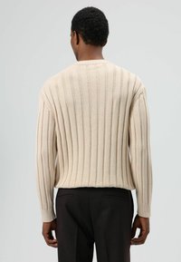 Beige geribbelde gebreide trui met lange mouwen, voorzien van een ronde hals en een textuurpatroon, gecombineerd met zwarte broek.