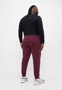 Camisa negra de manga larga combinada con pantalones de chándal burdeos que cuentan con una cintura elástica y puños ribeteados; zapatos deportivos grises completan el conjunto.
