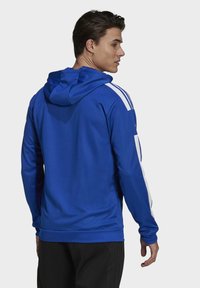 Sudadera azul fabricada en un material suave, con rayas blancas en los hombros, capucha con cordón y un corte relajado con un dobladillo ajustable.