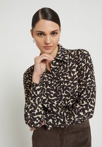 Langemouwige overhemden met een zwart en crèmekleurig abstract patroon, een kraagdetail en bruine knopen, gemaakt van een lichtgewicht stof.