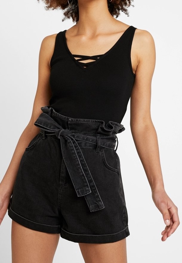 Débardeur noir côtelé avec un col en V présentant des détails entrecroisés, associé à un short en denim noir taille haute avec une ceinture à volants.