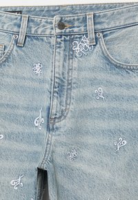 Lichtblauwe spijkerbroek met witte geborduurde krullen, voorzien van voorzakken, een knoopsluiting en contrasterende stiksels.