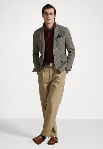 Veste grise texturée sur un polo bordeaux, pantalon beige et mocassins marron. Le mouchoir de poche ajoute du détail. Des lunettes complètent le look.