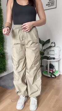 Beige, leichte Nylonhosen mit elastischem Bund und Seitentaschen. Schmal zulaufende Beine und eine glatte Textur. Getragen mit weißen Sneakers.