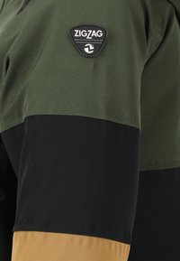 Korte mouwshirt in groen, zwart en bruin. Bevat een driehoeklogo patch op de borst. Glad van textuur met een kleurblokontwerp.