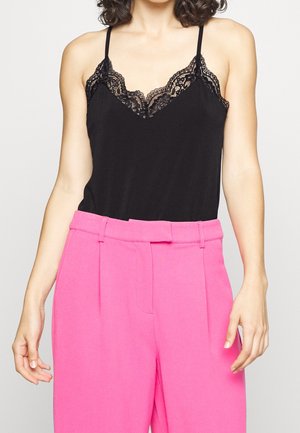 Camiseta negra sin mangas con detalles de encaje, combinada con pantalones de tiro alto en un brillante tono rosa, con un corte frontal plano y un ajuste estructurado.
