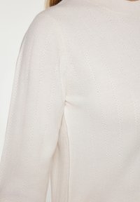Pulover usor, dintr-un tricot cu model canelat, de culoare roz pal, cu dungi verticale subtile si guler inalt. Textura moale cu mici detalii de broderie.